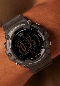 Montre numérique Casio avec un cadran noir, un boîtier en plastique gris et un bracelet. Affiche l'heure : 20h35. Comprend des boutons pour la lumière, les alarmes et les réglages de mode.