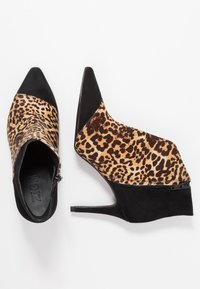 Par de botas de tobillo de mujer con punta afilada, estampado de leopardo y tacón de ante negro, cremallera lateral y tacón de aguja sobre fondo blanco.