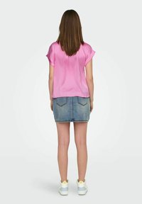 Růžový saténový top s krátkými ohrnutými rukávy, doplněný o úzkou džínsovou sukni a bílé tenisky s modrými a žlutými akcenty.