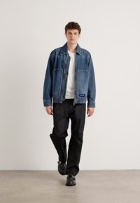 Jachetă din denim de un albastru mediu, cu o croială lejeră, având două buzunare frontale și cusături în contrast. Asortată cu pantaloni negri și pantofi.