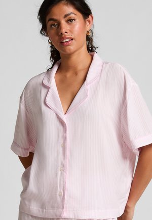 Woman wearing light pink, short-sleeve button-up pajama top with subtle vertical stripes and notched collar against plain background.