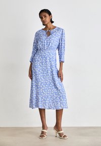 Rochie midi albastră cu un model abstract alb, mâneci lungi, guler legat și talie elastică. Țesătură netedă și siluetă fluidă.