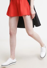 Weiße Leder-Schnürschuhe mit durchbrochenem Design, kombiniert mit einem roten ausgestellten Rock. Die Schuhe haben eine kontrastierende schwarze Sohle.