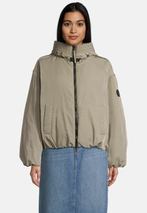 Lichtbeige bomberjack met hoge kraag, rits sluiting en elastische tailleband. Heeft twee zijzakken en een zwart rond accent op de mouw.