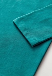 Türkisfarbenes Baumwollhemd mit gefaltetem Ärmel und glatter Textur, mit sauberer Naht entlang der Kanten.