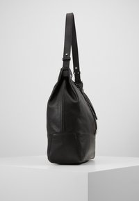 Svart läderhandväska med texturerad yta, en lång justerbar rem och dragkedjestängning. Har en strukturerad kropp och platt botten för stabilitet.