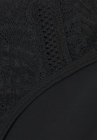 Lingerie noire avec un panneau en dentelle texturée comportant des motifs intriqués, complété par un tissu en noir uni, lisse et mat.