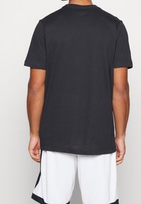 Camiseta negra de manga corta hecha de algodón suave, con un cuello redondo, que presenta un diseño sencillo y un corte relajado, combinada con pantalones cortos blancos.