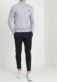 Grå polotröja med ribbad textur, svart logotypaccent, kombinerad med slim-fit mörkblå randiga byxor och vita sneakers.