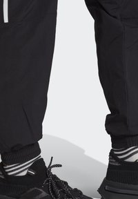 Mustat urheiluhousut joustavilla hihansuilla ja heijastavilla yksityiskohdilla, yhdistettyinä mustiin kenkiin ja raidallisiin mustiin ja valkoisiin sukkiin.