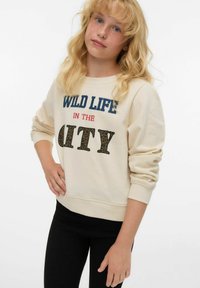 Krämfärgad sweatshirt med djärv text "WILD LIFE IN THE CITY" i leopardmönstrade bokstäver. Ribbad mudd och fåll, bärs med svarta leggings.
