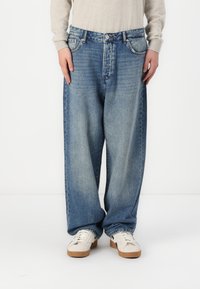 Lysblå vide jeans lavet af denim med en falmet finish, der har fem lommer og lukning med knap, stylet med hvide sneakers.