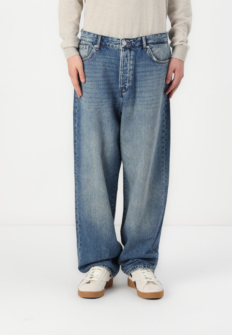 Lysblå vide jeans lavet af denim med en falmet finish, der har fem lommer og lukning med knap, stylet med hvide sneakers.