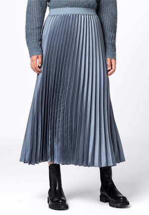 Jupe midi plissée en dégradé de bleu clair à bleu foncé en satin, avec une large ceinture. Portée avec des bottines noires.