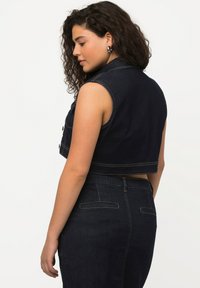 Beskarvad denimväst i mörkblått med kontrasterande gul söm, med krage och knappstängning, i kombination med högmidjade denim.