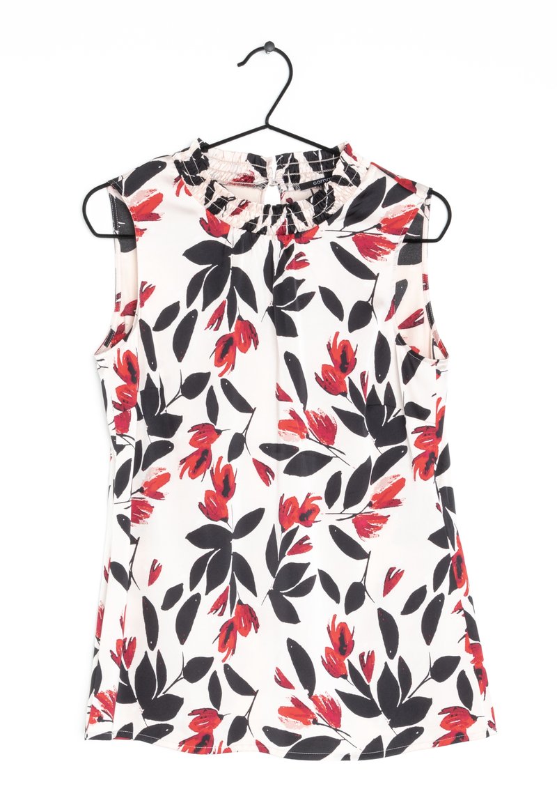 Haut sans manches à imprimé floral avec un col à volants, présentant des fleurs rouges et noires sur fond blanc. Tissu léger, avec une coupe décontractée.