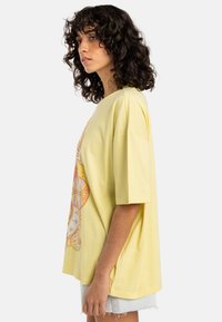 Gul oversized t-shirt lavet af bomuld, prydet med et farverigt grafisk design på forsiden. Skåret med korte ærmer og en afslappet pasform.