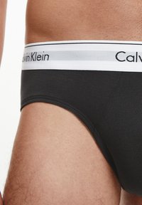 Slip di cotone nero con elastico bianco e grigio che presenta il logo "Calvin Klein". Tessuto liscio e vestibilità aderente.