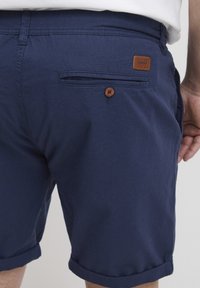 Mørkeblå vevde shorts med slim passform. Har en knappet lomme, oppbrettede ermer og en lær merke på baksiden. Glatt tekstur.