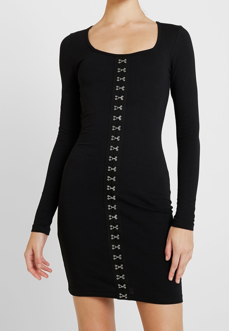 Černé dlouhé šaty s obdélníkovým výstřihem, v přední části mají středový panel zdobený stříbrnými kovovými detaily.