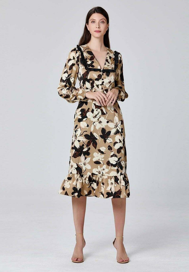 Robe midi florale avec une base beige ornée de fleurs noires et blanches, ourlet à volants et décolleté en V. Manches longues avec détails froncés.