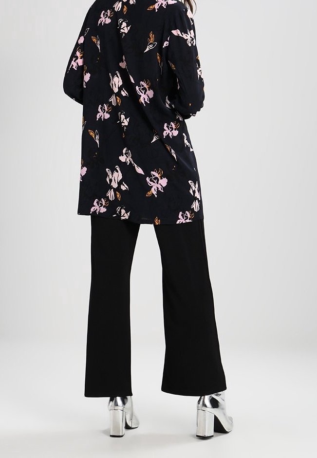 Blazer nero a fiori con motivi rosa e arancioni, abbinato a pantaloni neri a gamba larga e stivaletti con tacco a blocco argentati.