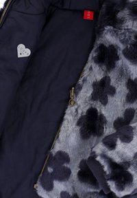 Blauwe en zwarte gevlekte nepbontjas met een gedeeltelijk geopende rits, die een donkerblauwe voering toont met een hartvormig label.