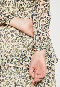 Košile na knoflíky z lehkého, průhledného materiálu s pastelovým leopardím potiskem. Má nařasený výstřih a dlouhé rukávy s knoflíkovými manžetami.