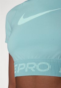 Top atlético recortado de color azul claro hecho de material elástico. Presenta un dobladillo acanalado con "PRO" en blanco y un logo de Nike en blanco en el pecho.