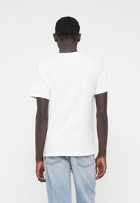 Balta medvilninė marškinėliai su apvalia iškirpte ir trumpomis rankovėmis, tiesiu apvadu. Dėvimi su šviesiai mėlynais džinsais.