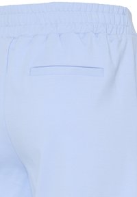 Pantalon bleu clair avec une taille élastique et une poche passepoilée horizontale sur le côté droit à l'arrière.