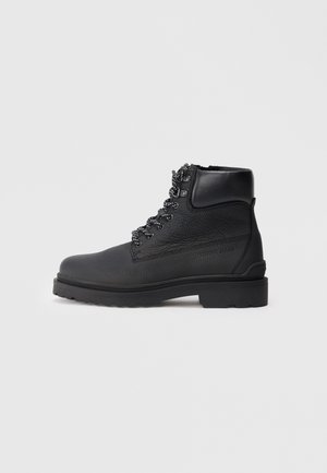 Black leather boot with textured finish, round toe, ankle height, and metallic hardware for laces. Chunky, durable rubber sole.