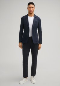 Marineblauwe textuur blazer met twee voorzakken, witte ronde hals shirt, slim-fit donkere broek en witte sneakers. Eenvoudig, modern design.