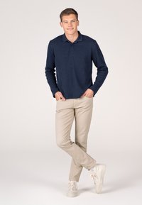 Marineblaue Langarm-Polohemden mit strukturiertem Muster, kombiniert mit beigen Hosen und hellen Sneakers, die ein lässiges Outfit ergeben.