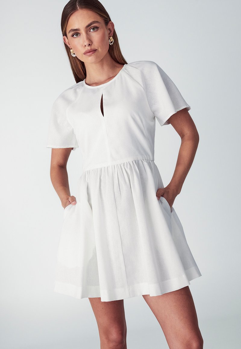 Biele šaty s krátkym rukávom a okrúhlym výstrihom, so predným výrezom, elastickým pásom a bočnými vreckami. Hladká látka s voľnou sukňou.