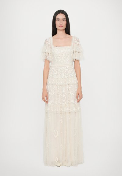 Robe longue en ivoire avec des manches bouffantes transparentes, broderies florales intriquées et jupe en tulle superposée. Encolure carrée et textures subtiles.