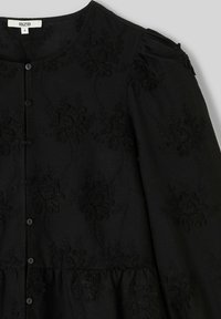 Robe noire boutonnée ornée de motifs floraux brodés, manches froncées et design à étages pour une texture et des détails supplémentaires.