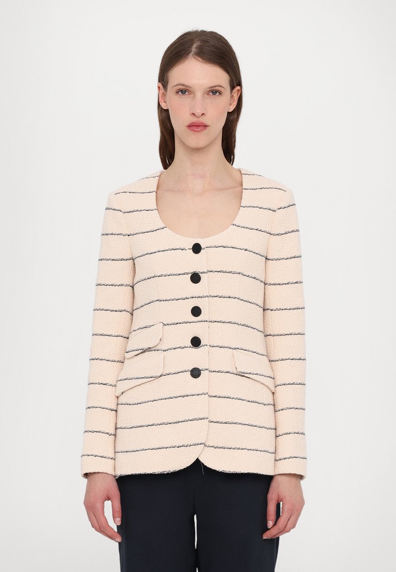 Cremefarvet jakke med sorte vandrette striber, rund halsudskæring, fem sorte knapper og to forlommer. Tekstureret stof.