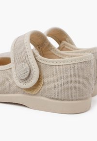 Zapatos de lona beige con una superficie texturizada, que cuentan con una correa de gancho y bucle y un diseño de punta redonda. Suela de goma para agarre y soporte.