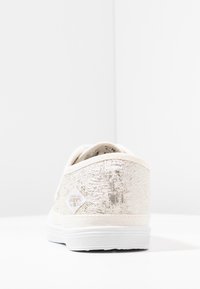 Baskets en textile beige avec une finition texturée, semelle en caoutchouc blanc et un patch en forme de diamant sur le côté. Design à profil bas.