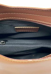 Interno di una borsa in pelle marrone con una superficie testurizzata, dotata di una tasca con zip e cuciture a contrasto lungo i bordi.