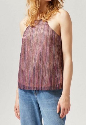 Kobieta w bezrękawnikowej bluzce z wysokim dekoltem w purpurowe i metaliczne paski, w zestawieniu z niebieskimi dżinsami na neutralnym tle.