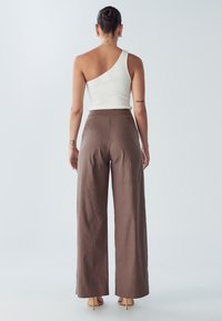 Asymetryczny biały prążkowany top na ramiączkach w połączeniu z brązowymi, szerokimi spodniami z wysokim stanem. Gładka tekstura, minimalistyczny design, neutralna paleta kolorów.