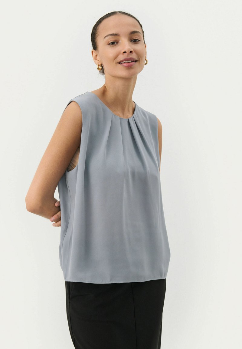 Gray sleeveless top with a round neckline, soft draping, and pleated front detail, paired with black bottoms. Smooth, lightweight fabric.