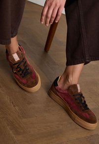 Sneakers made of mixed materials featuring burgundy and brown suede, black laces, and a thick beige sole; leopard print accents on the sides.