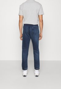 Šedé polo tričko s krátkým rukávem na osobě, spárované s tmavomodrými džíny, které mají zadní kapsu a ohrnuté nohavice, doplněné bílými teniskami.