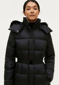 Zwarte gewatteerde winterjas met een hoge kraag, afneembare bonttrim, een ceintuur in de taille en twee zijzakken, met een glanzende afwerking en een doorstikte uitstraling.