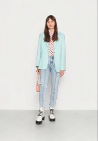 Blazer oversized verde menta, blusa com padrão de corações rosa, jeans azul claro, botas de combate com atacadores em preto e branco, e uma pequena bolsa rosa.