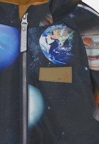 Färgglad rymdtema-jacka med planeter, stjärnor och galaxer. Mörk tyg med en slät textur och en brun läderlogotyp.