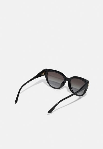 Lunettes de soleil noires avec un design œil de chat, verres dégradés et montures en acétate brillant avec des accents en métal doré sur les branches.